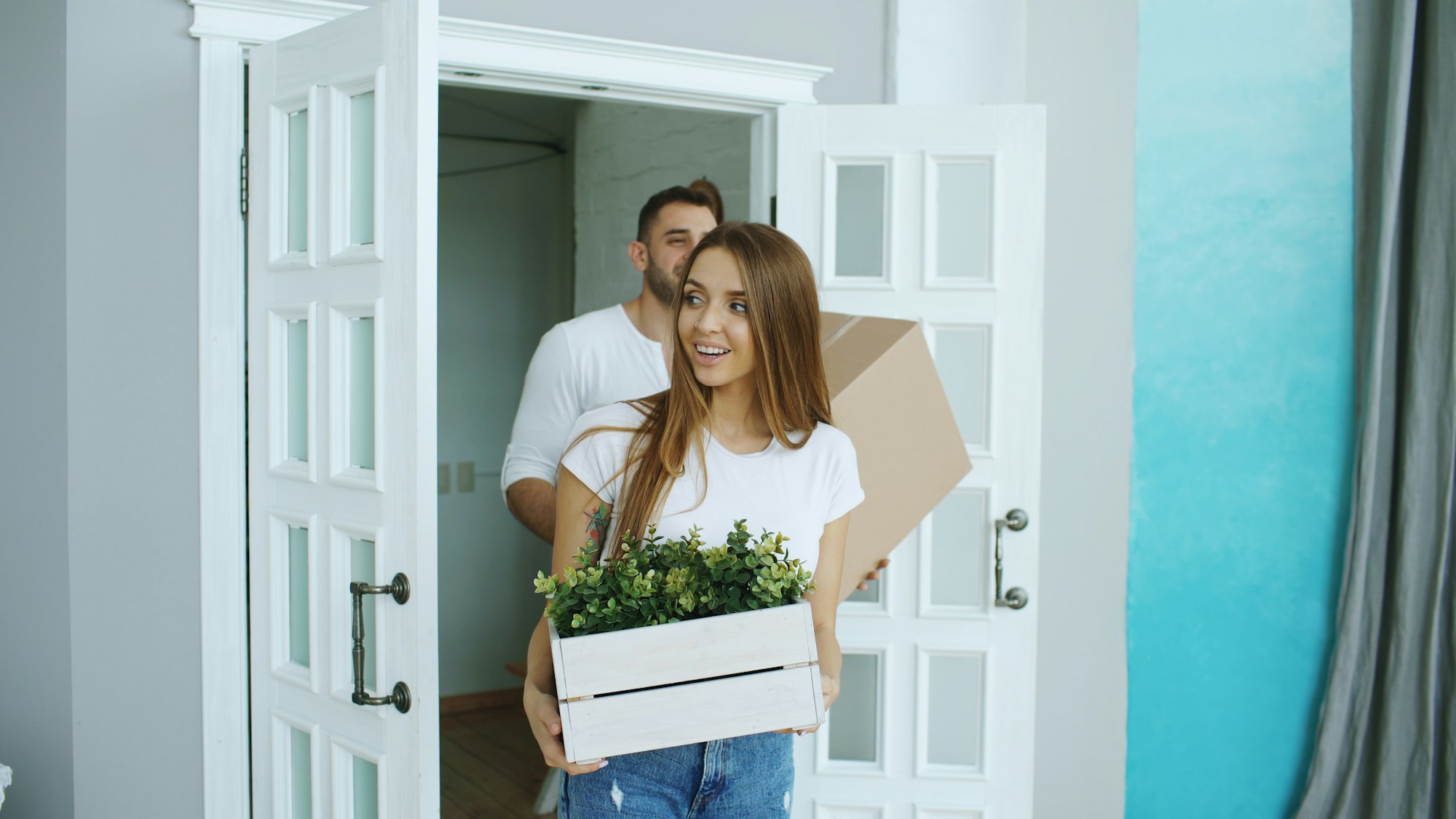 Happy couple walking through the front door of their new home carrying moving boxes