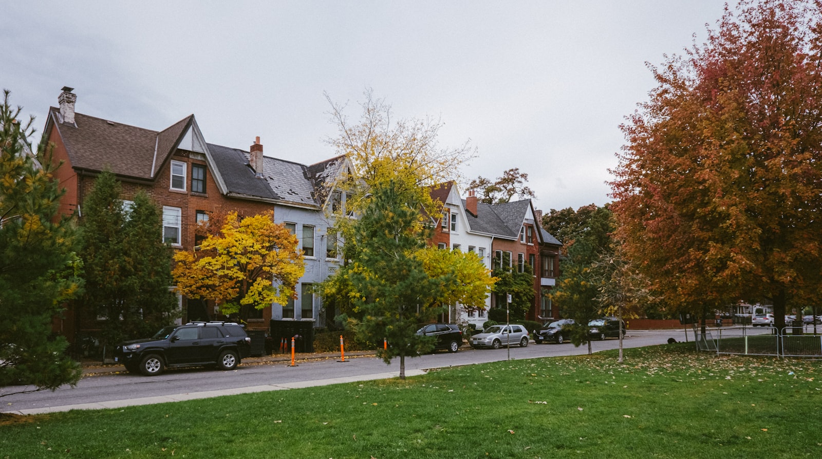 A row of attached brick houses along a residential street lined with autumn trees
