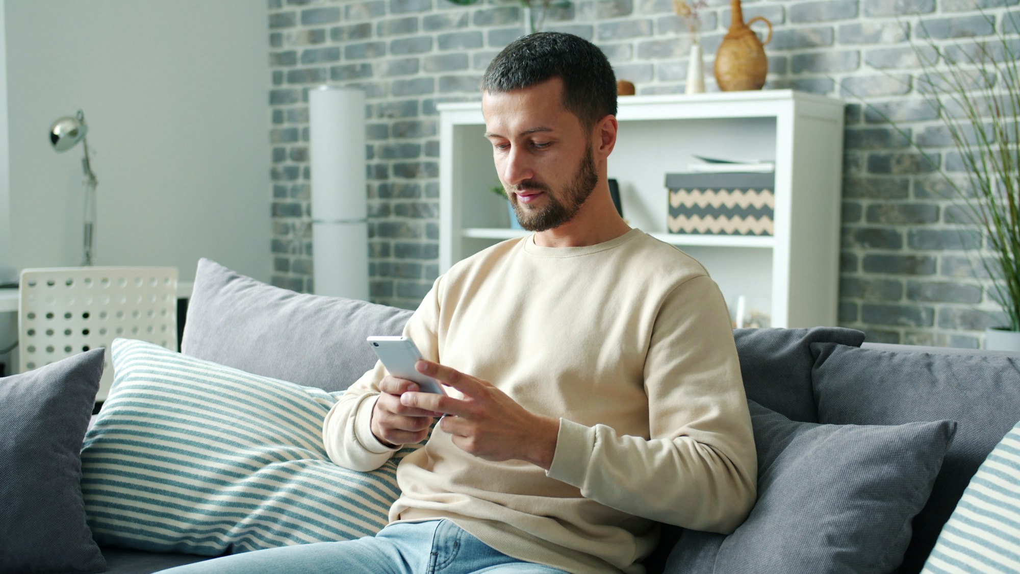 Man sitting on a couch checking real estate listings on his phone
