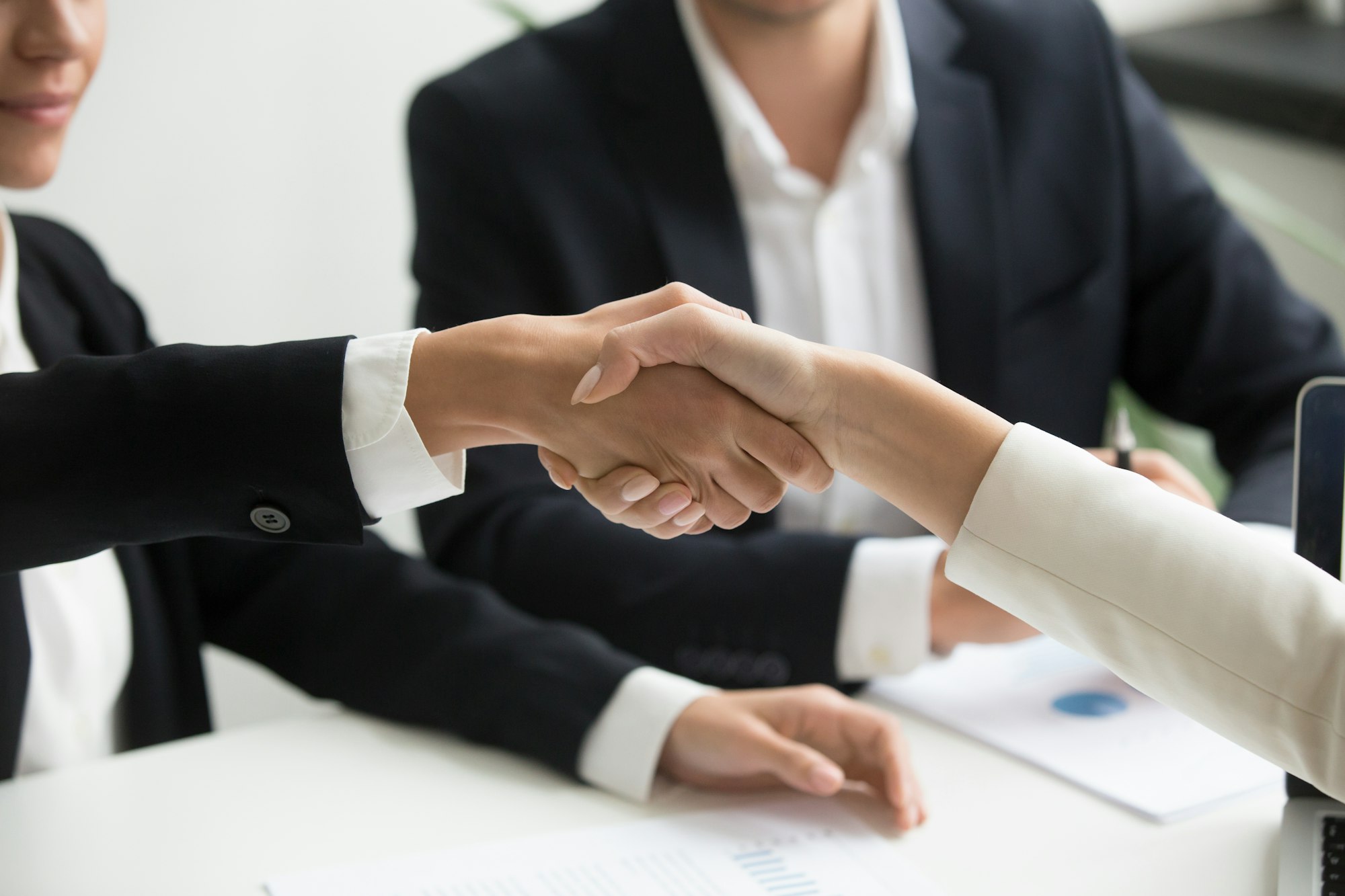 Two professionals shaking hands across a table in a bright office