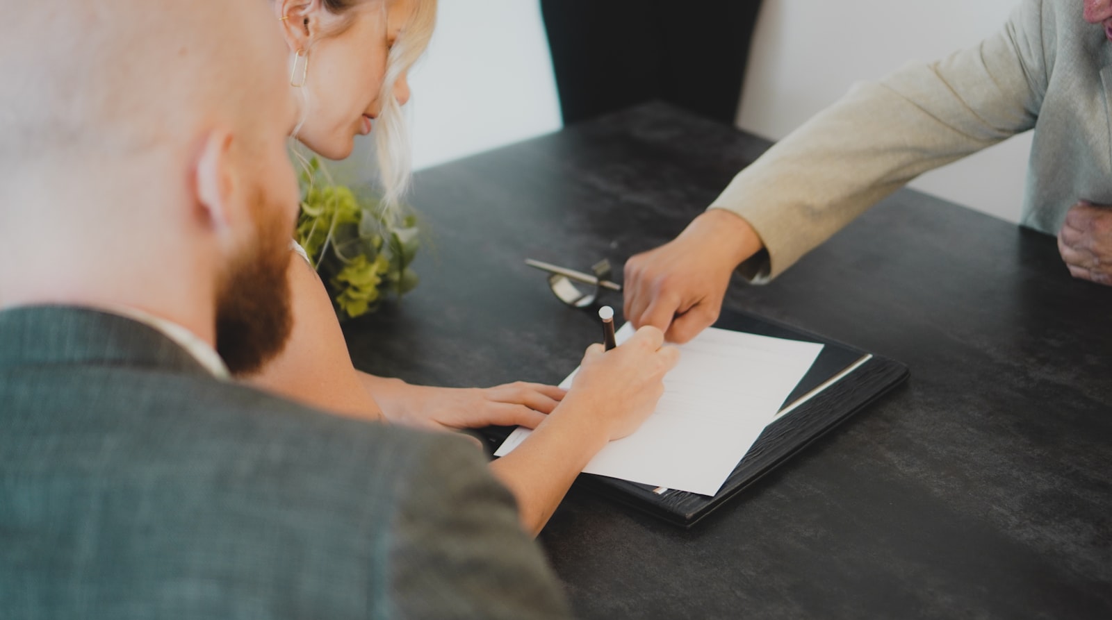 A buyer signing a real estate agreement at a table while an agent points to the signature line